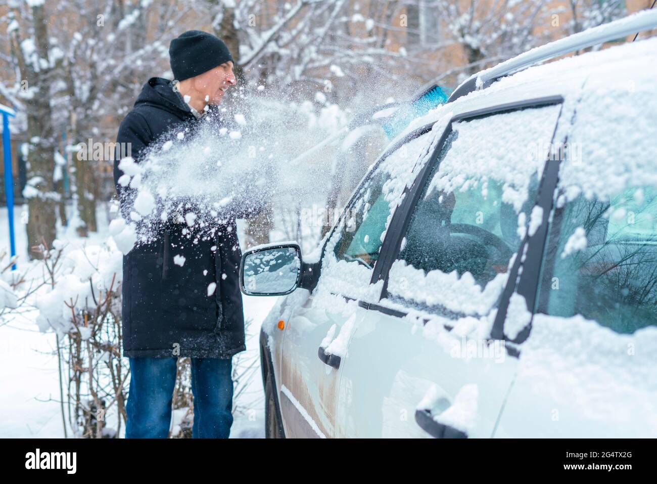adult male removing snow from car roof with brush in winter season