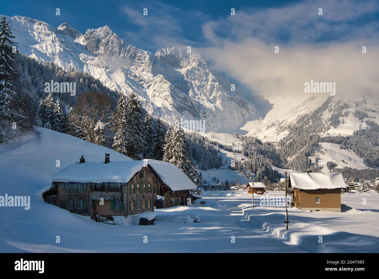 Winter landscape of a house and hut in winter snows with a lovely mountain backdrop with blue sky, at Engelberg in Obwalden canton, Switzerland Stock Photo