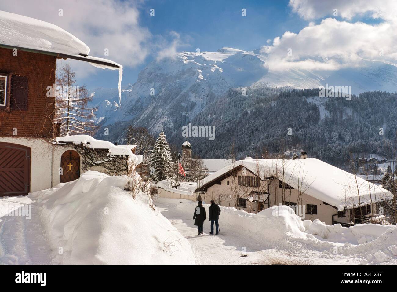 A winter scene of houses, chalets and rooftops covered in a thick layer of snow, also a couple walk in Engelberg, Obwalden canton, central Switzerland Stock Photo