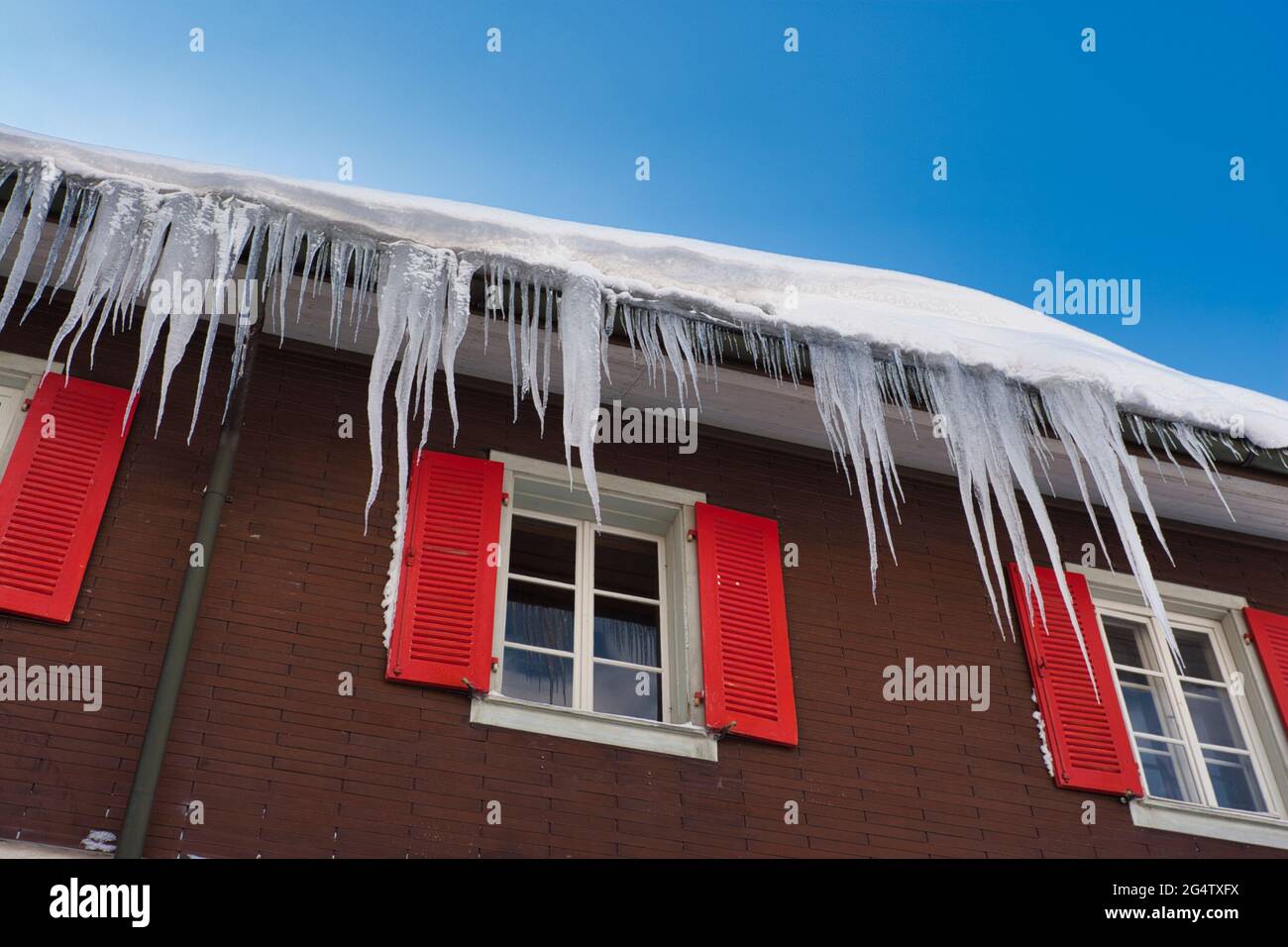 Large icicles hang from the roof and gutters of a typical Swiss house with shuttered windows in Engelberg, central Switzerland Stock Photo