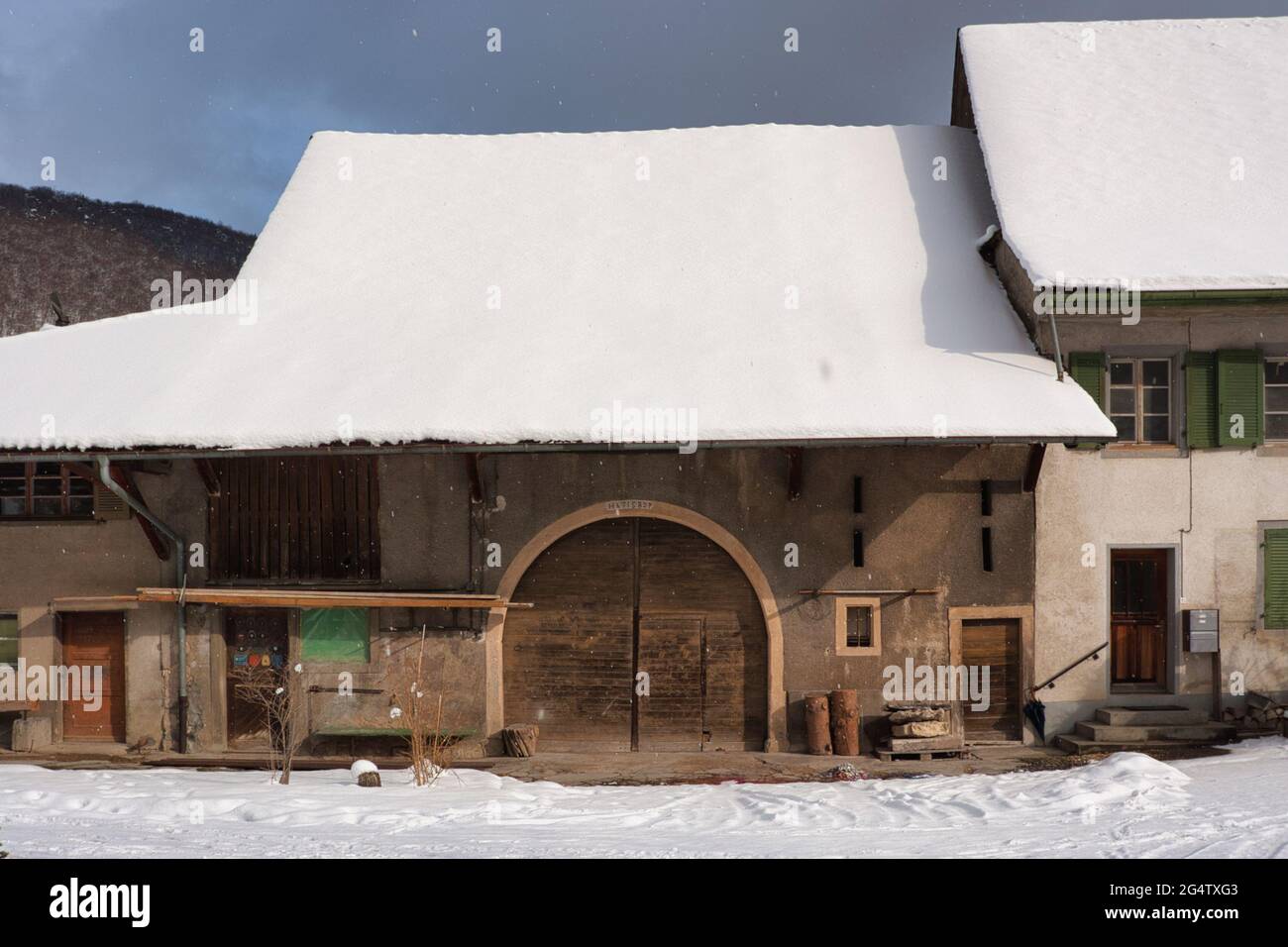 An old barn with large arched doorway and snow covered roof in the village of Oberdorf, Switzerland Stock Photo