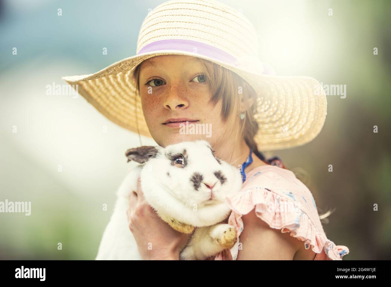 Young kid in a hat holding a scared rabbit in hands. Rabbit is scared ...
