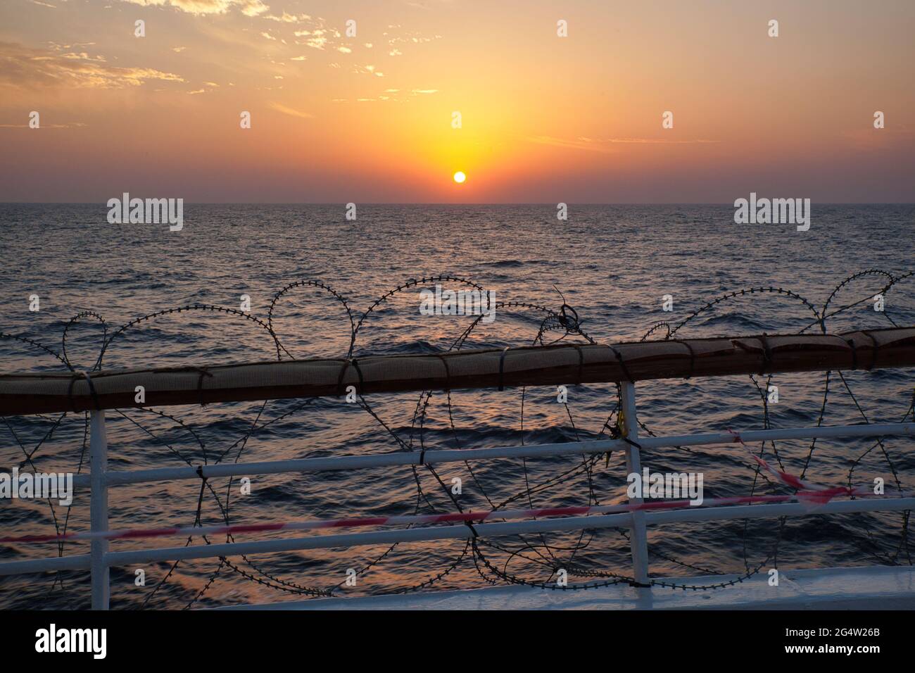 Sunset over the Indian Ocean from stern of a ship with the railing wound with razor wire in case of attack by pirates or terrorists to stop boarding Stock Photo