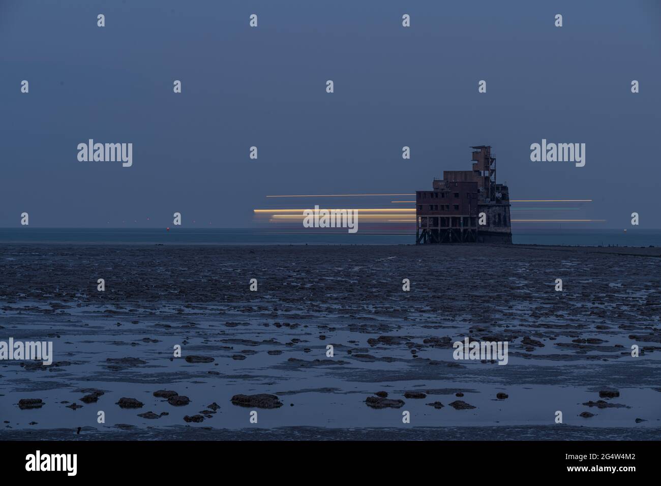 Blurred lights of a Ship moving behind Grain fort at dusk Stock Photo