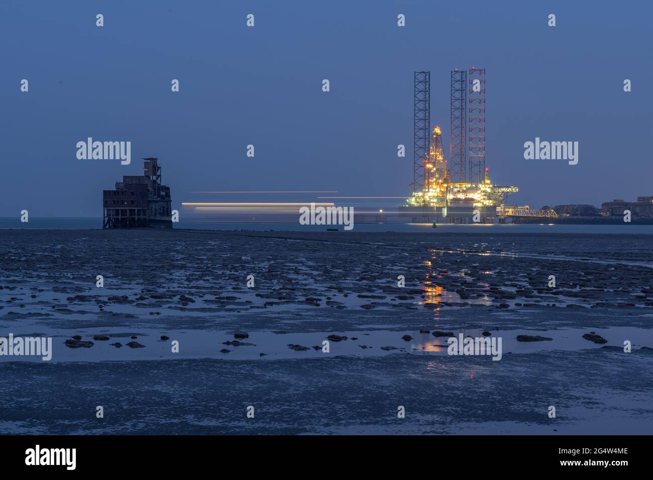 Blurred lights of a Ship moving behind  Grain fort in the Swale with drilling rig moored at Sheerness in the background taken at night. Stock Photo