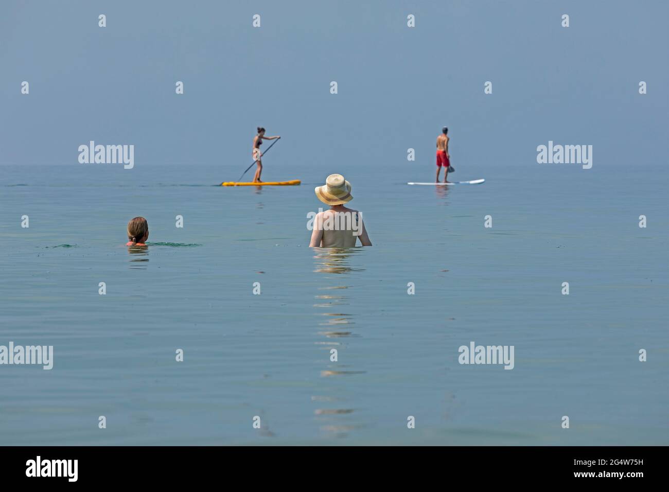 two women watching two people doing stand-up paddle boarding, Wustrow, Fischland, Mecklenburg-West Pomerania, Germany Stock Photo