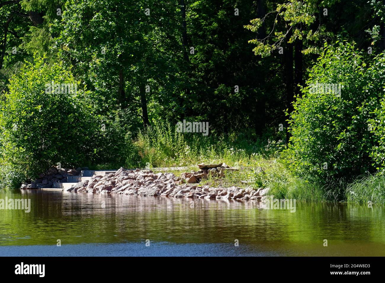 Stone steps on a rocky shore, descending to the water of a small pond in the Monrepos Park in the city of Vyborg. Stock Photo