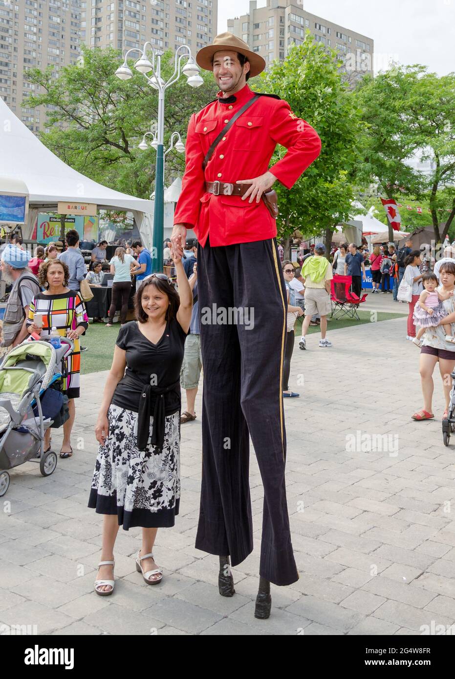 Canadian mountie on a Canada Day holiday on stilts poses with a smiling woman for tourist photographs. Stock Photo