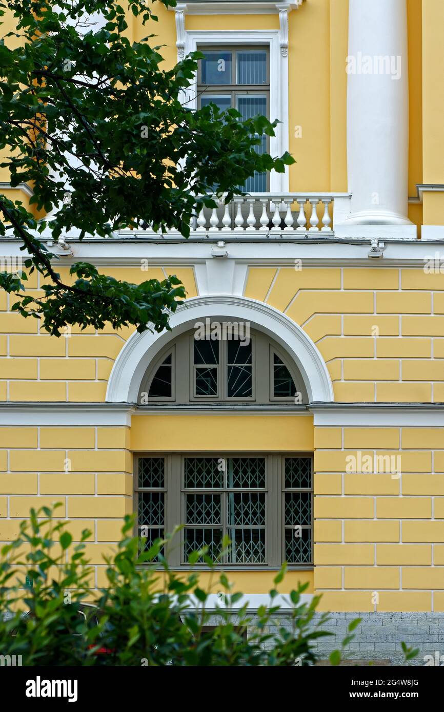 Arched window and a rectangular window with a balcony and white columns against a yellow wall. From a series of windows of St. Petersburg. Stock Photo