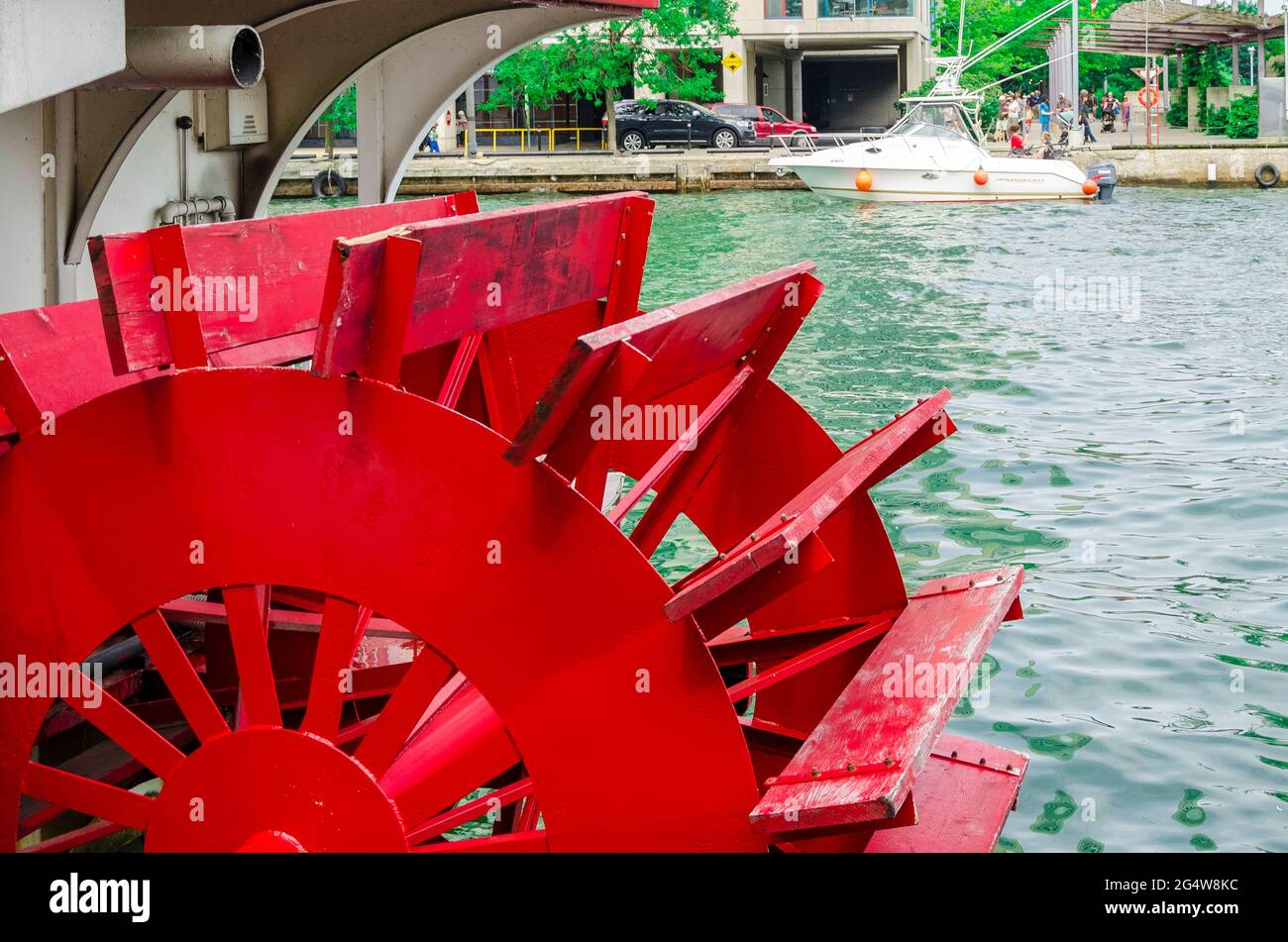 Close-up of a red paddle wheel of a paddle boat near a harbor with a steamer and a building in the background Stock Photo