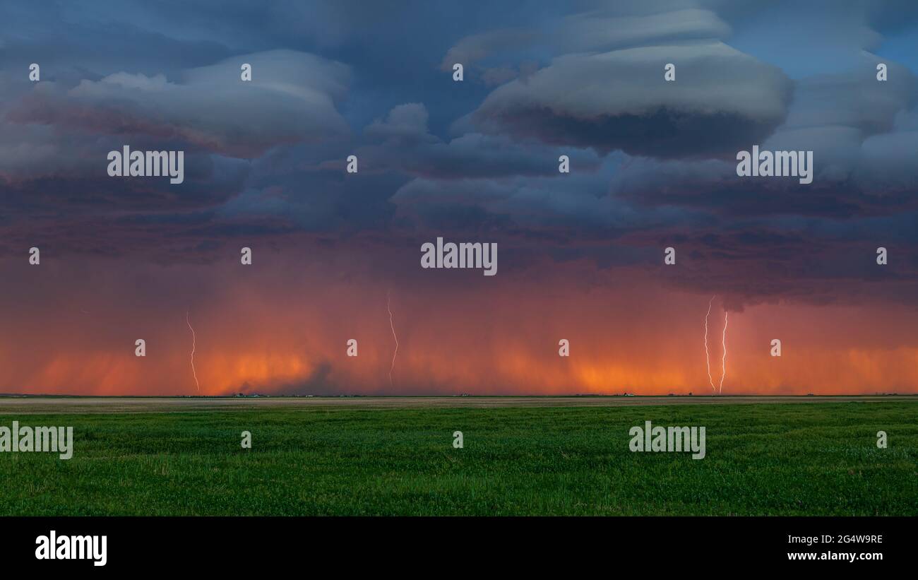 Multiple lightning bolts strike along the Colorado / Wyoming border at sunset with the orange glow of sunset seen on the horizon Stock Photo
