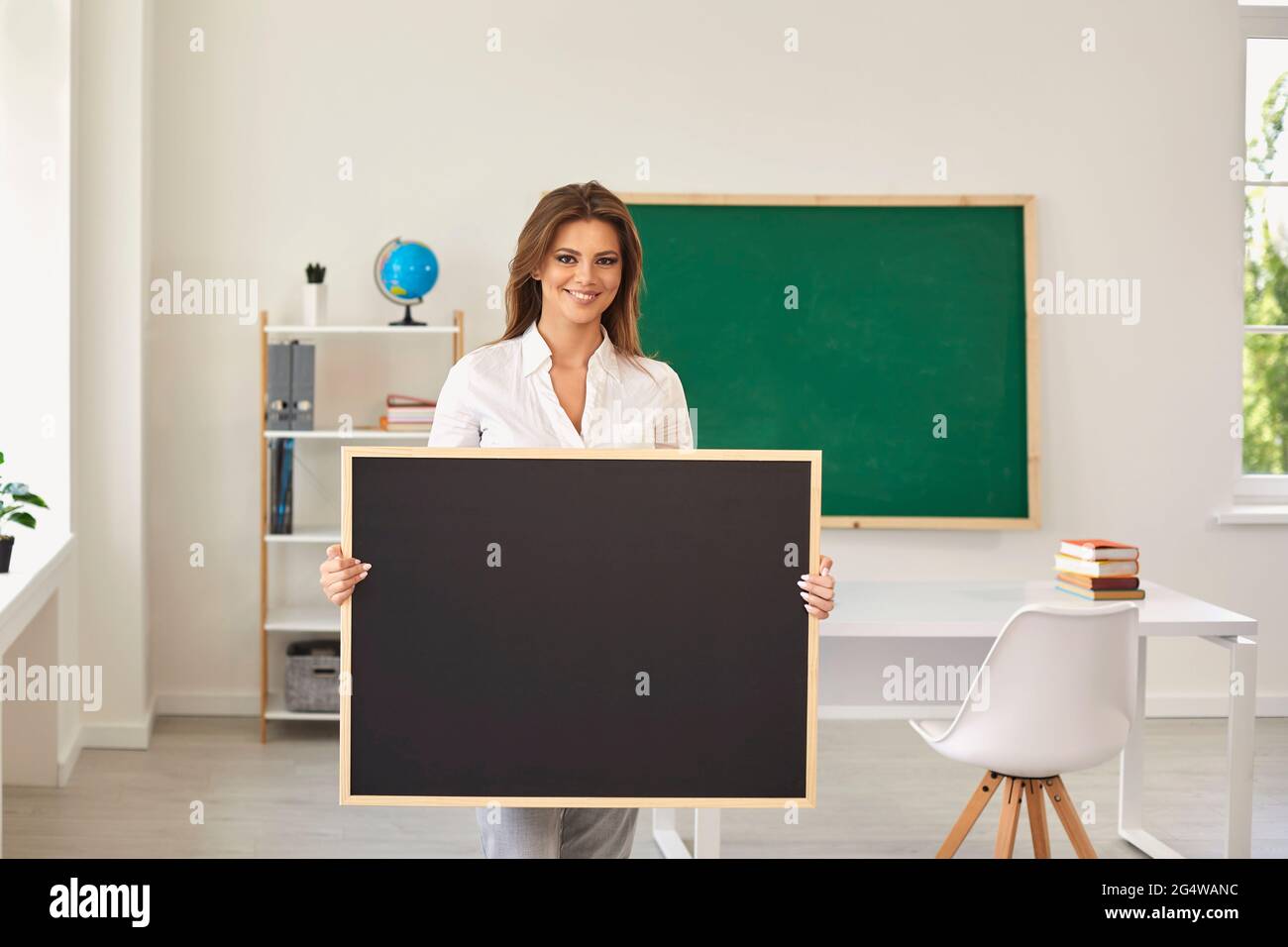 Teacher school. Smiling girl teacher holds a board for text with hands standing in class. Education Learning Concept. Stock Photo