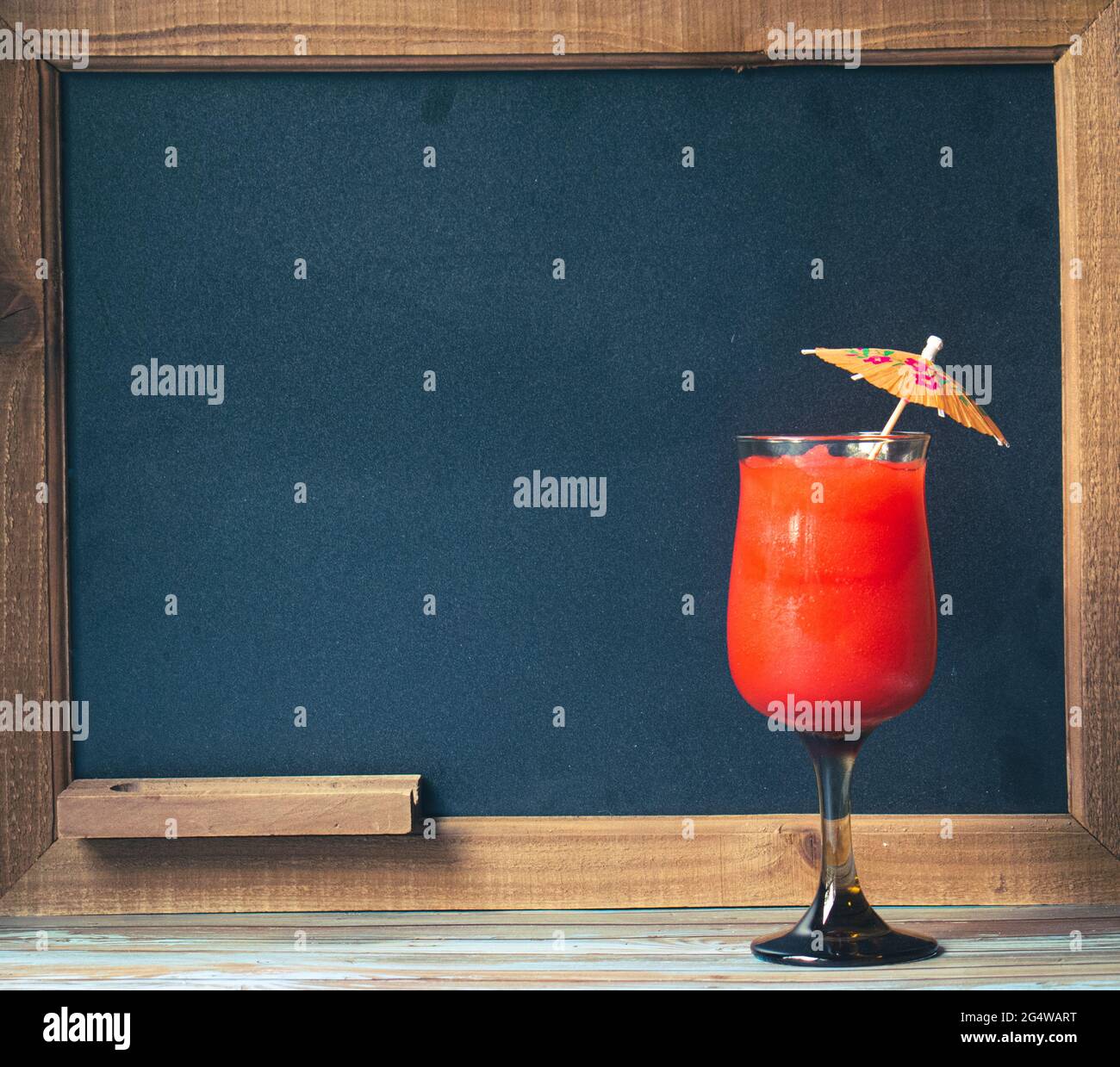Cocktail drink in front of chalkboard for the drink menu, with tropical wood table Stock Photo