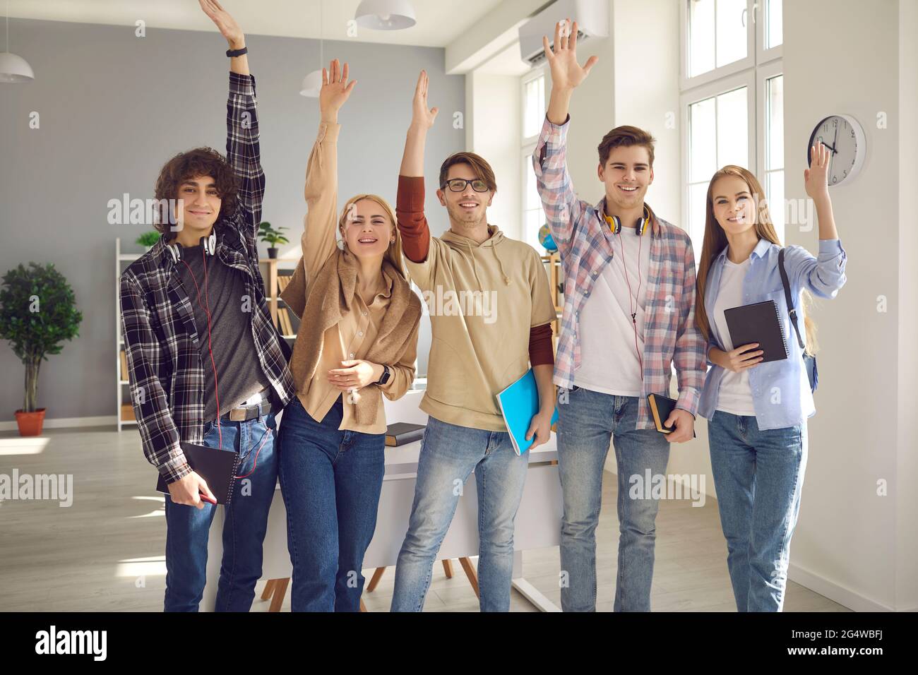 Group of happy smart students standing in classroom and raising hands ...