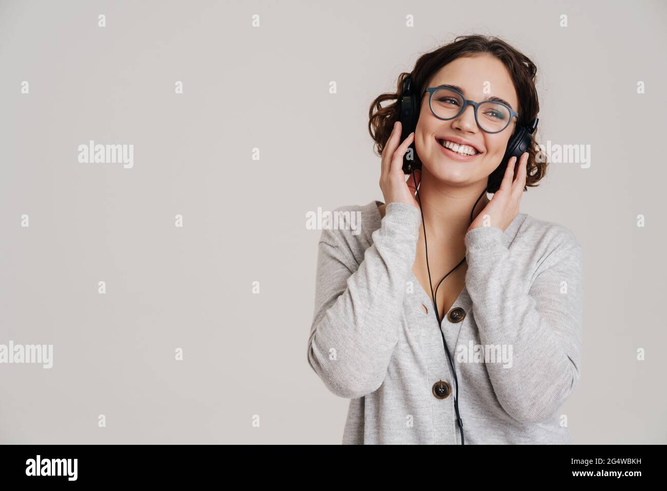 Lovely cheerful young woman listening to music with headphones isolated ...