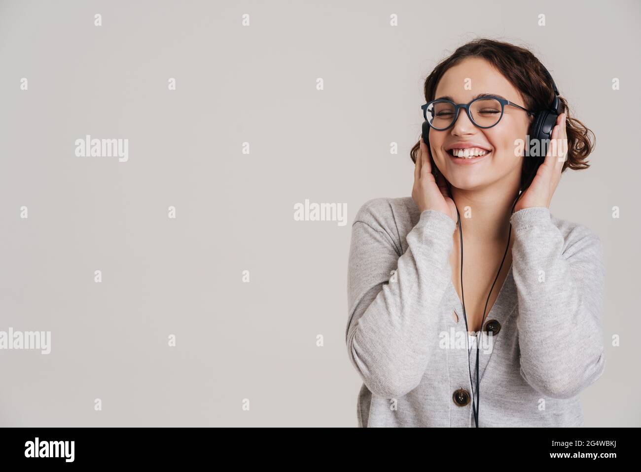 Lovely cheerful young woman listening to music with headphones isolated ...