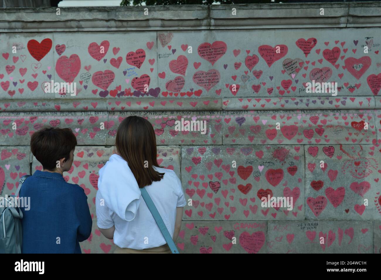London, UK. 23 June 2021. Two women reading the tributes written on The National COVID Memorial Wall covered in hand drawn love hearts. Stock Photo