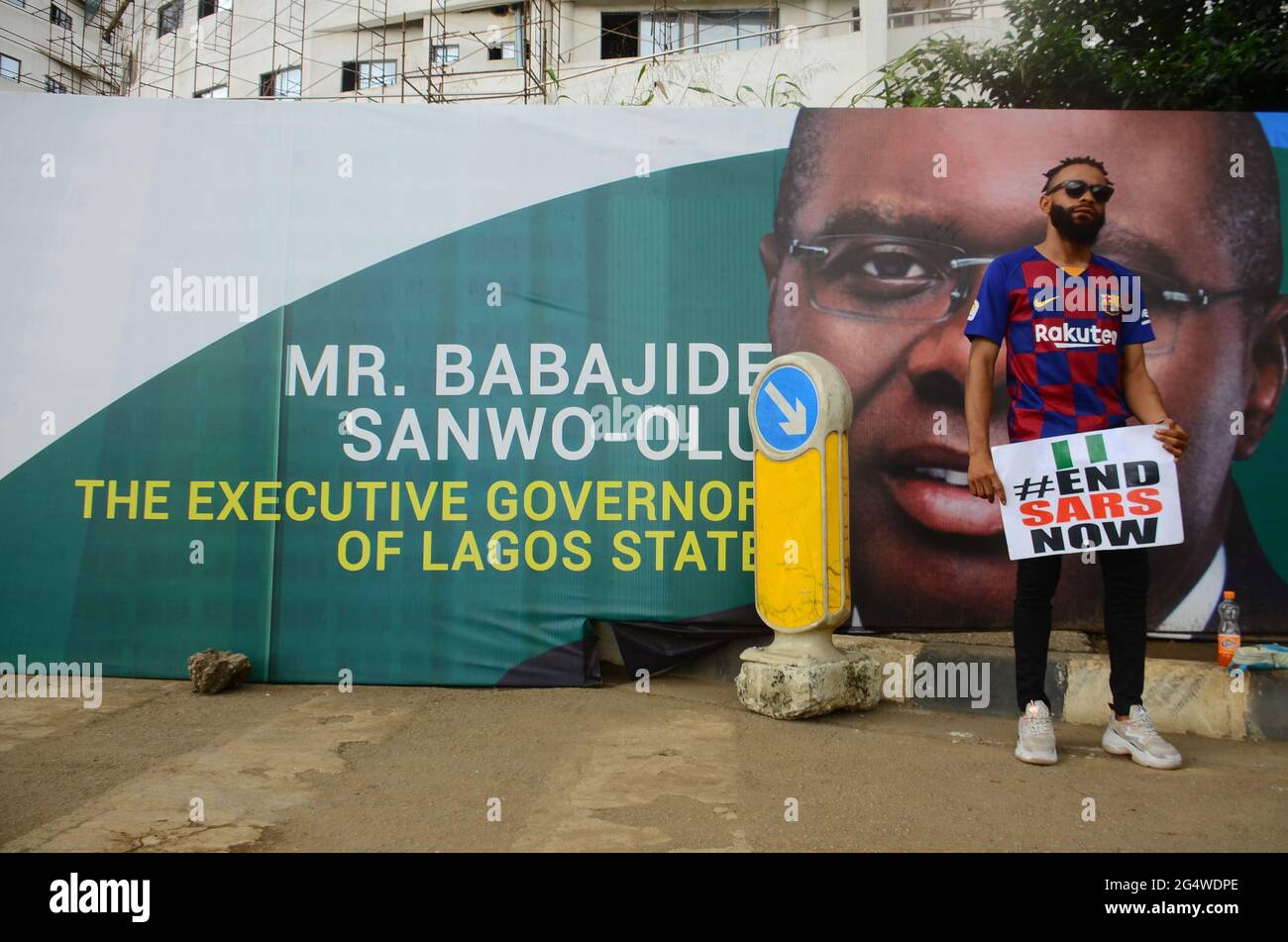 A youth protester of ENDSARS displaying his placards in front of a banner with the picture of the Lagos State Governor (Babajide Sonwo-Olu) at the ongoing protest against the harassment, killings and brutality of the Nigerian Police Force Unit called Special Anti-Robbery Squad (SARS) in the Lagos State House of Assembly. Lagos, Nigeria. Stock Photo