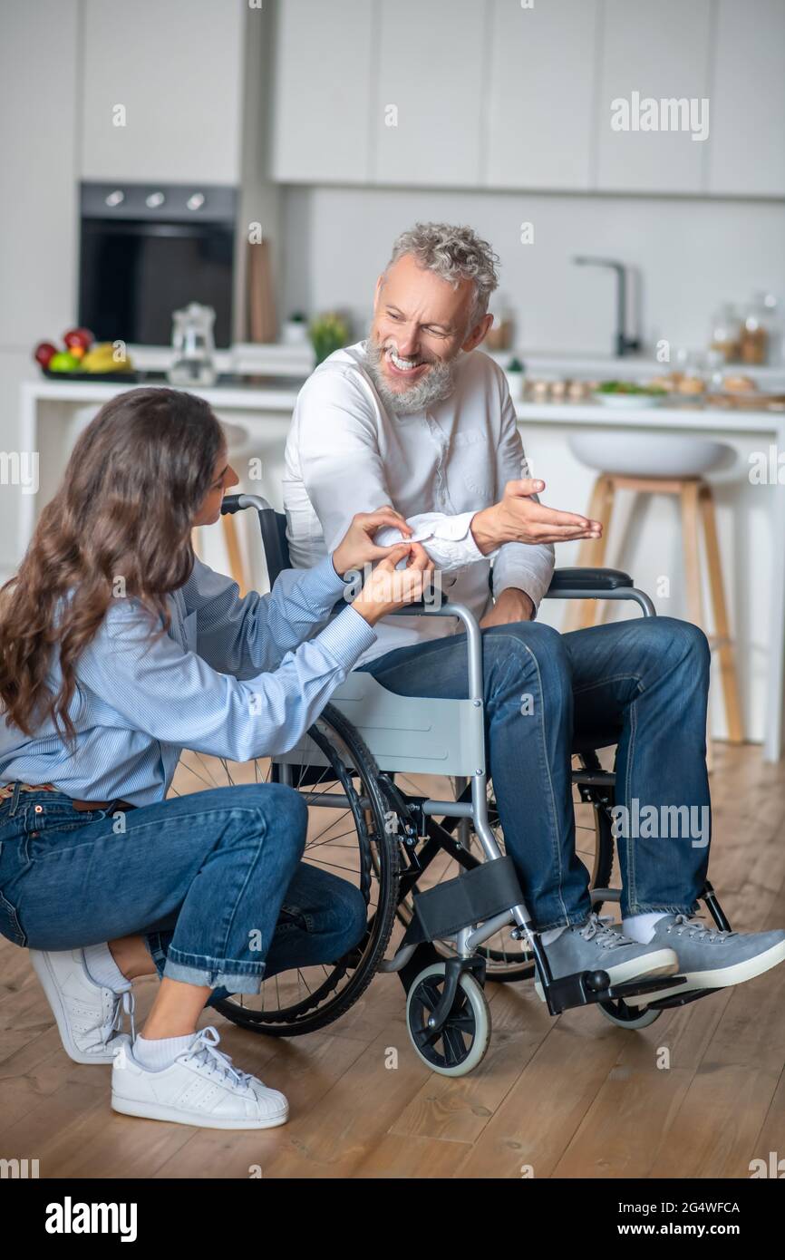 Pretty woman taking care about her handicapped husband and smiling nicely Stock Photo