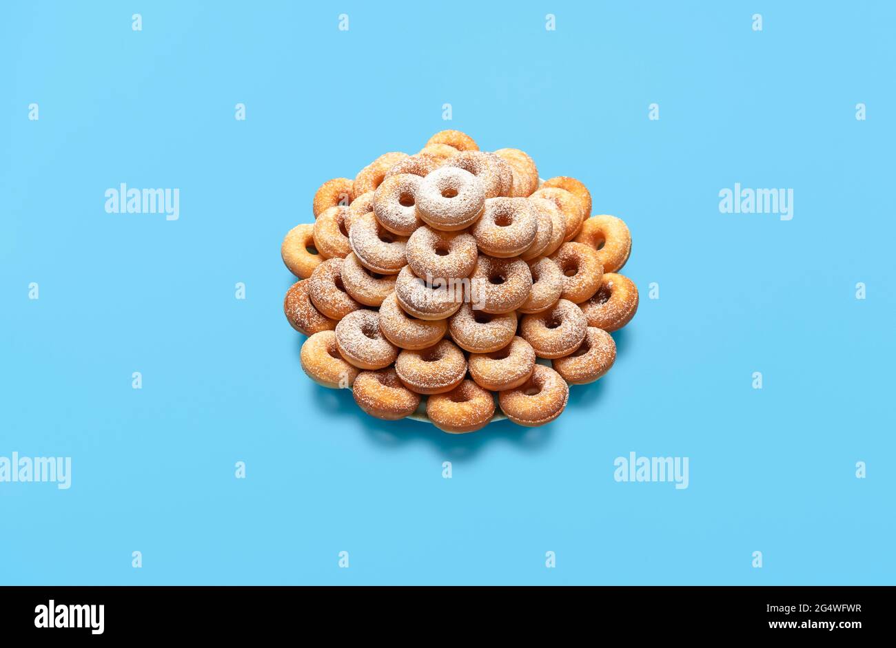 Homemade donuts with powder sugar, on a plate, isolated on a blue-colored background. Freshly baked mini doughnuts, ready to serve on a blue table. Stock Photo