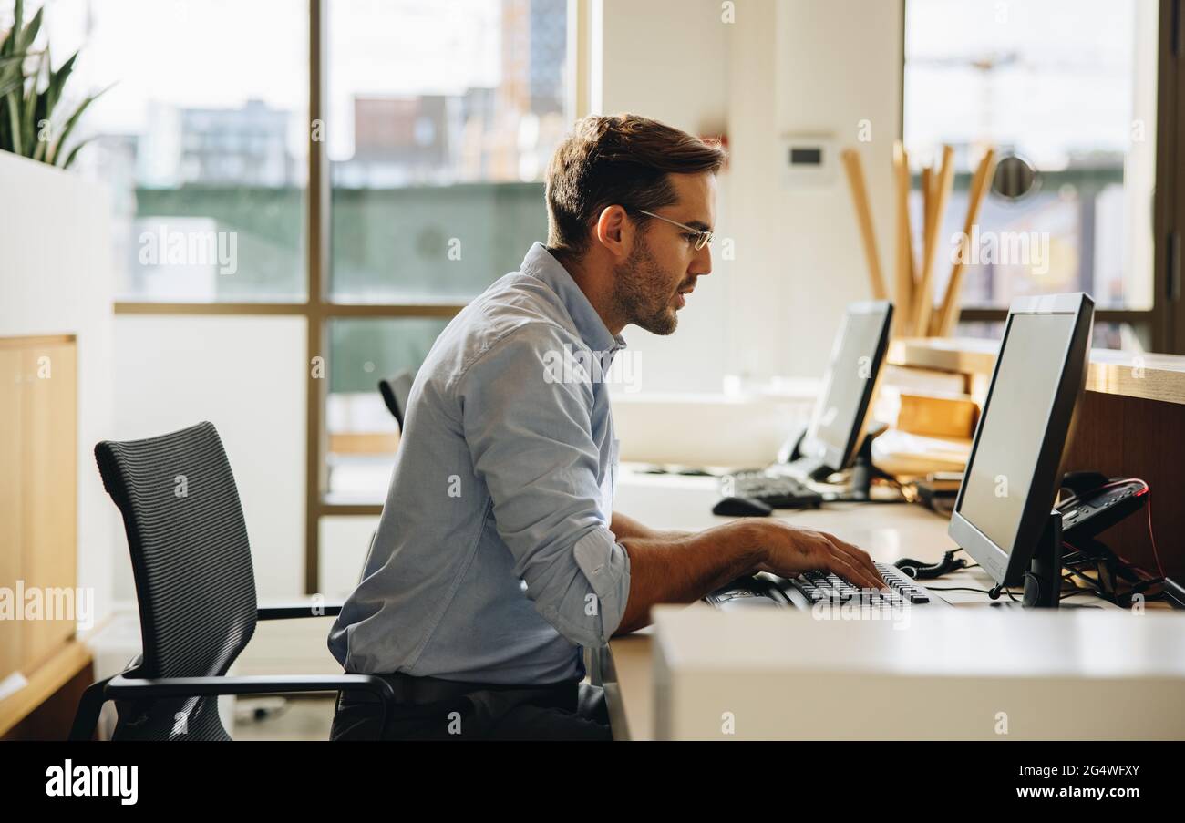 https://c8.alamy.com/comp/2G4WFXY/executive-looking-at-computer-screen-and-typing-on-keyboard-in-office-young-man-sitting-in-office-working-on-computer-2G4WFXY.jpg