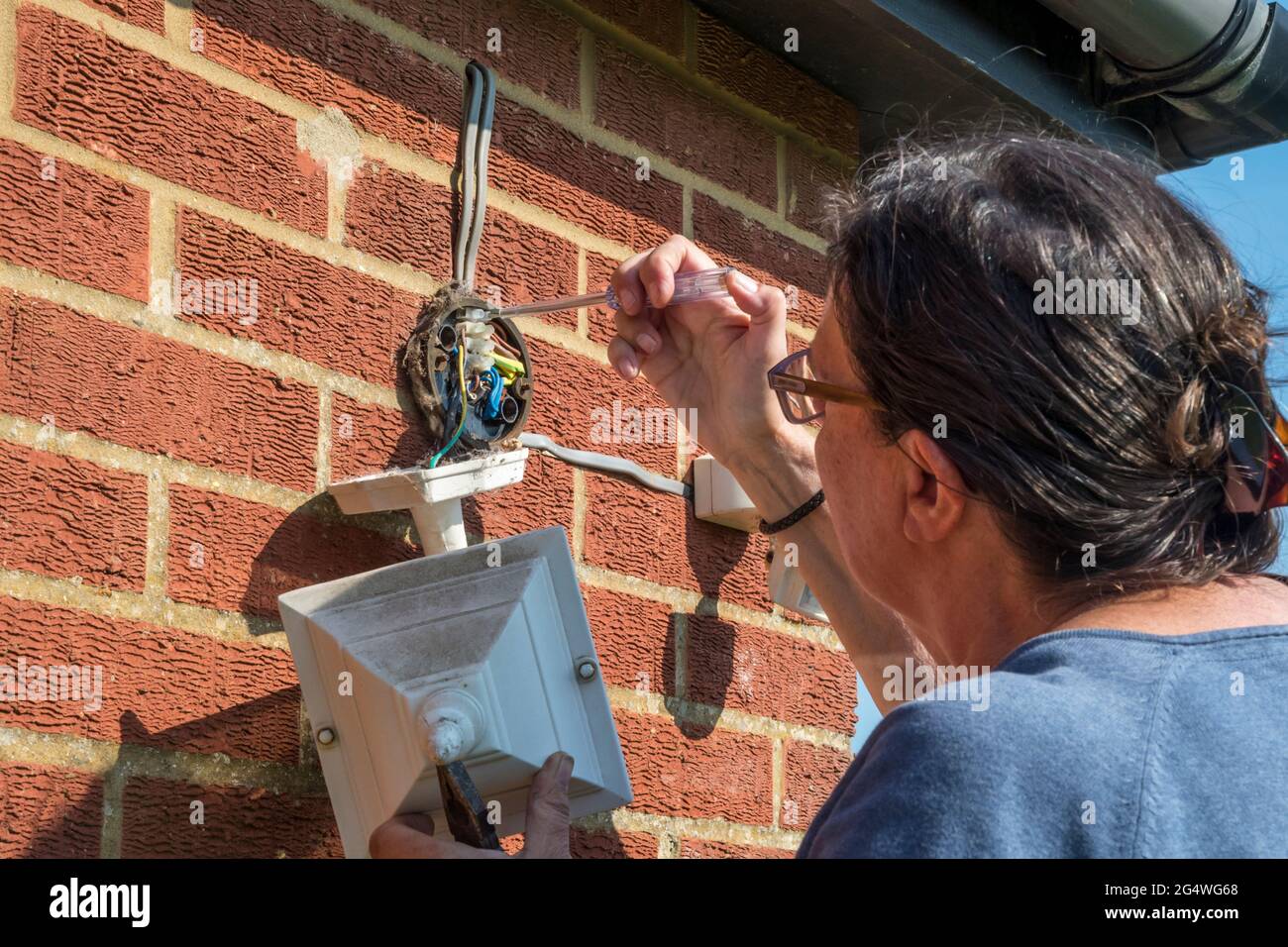 Woman fixing outside lights on an external wall. Stock Photo