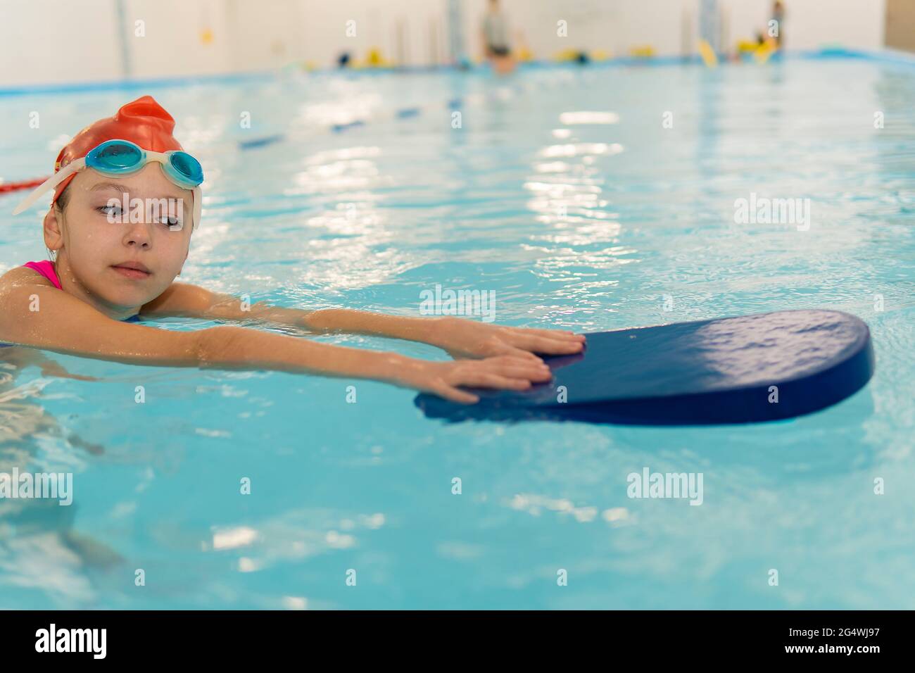 Happy little girl learning to swim with pool board. Sports and entertainment for children. Swimming competition. Healthy lifestyle from childhood. Stock Photo