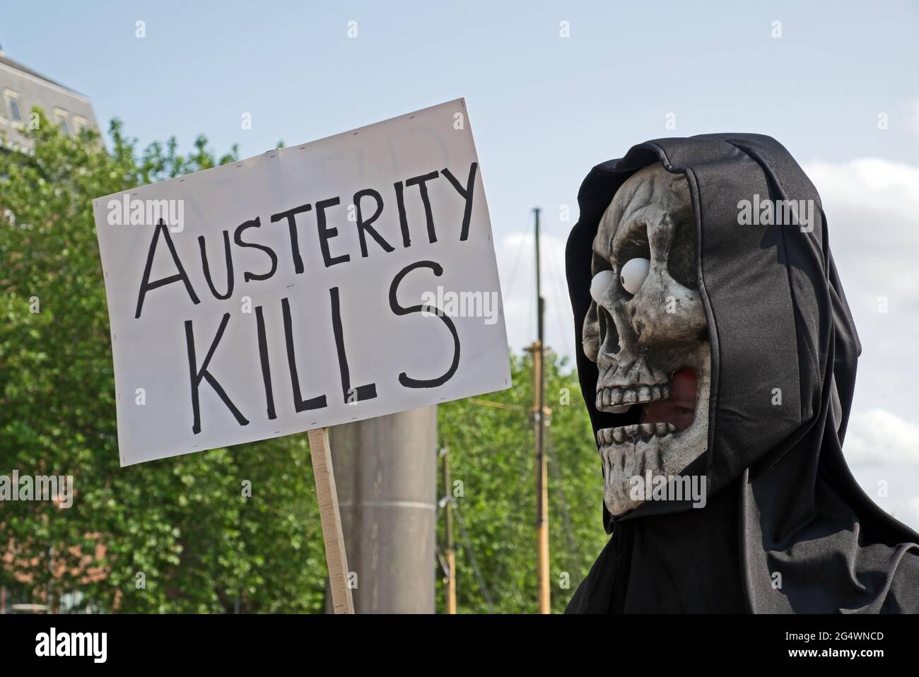 A masked anti-austerity demonstrator holds a placard with the slogan “AUSTERITY KILLS” in Bristol, UK on 8 July 2015 Stock Photo