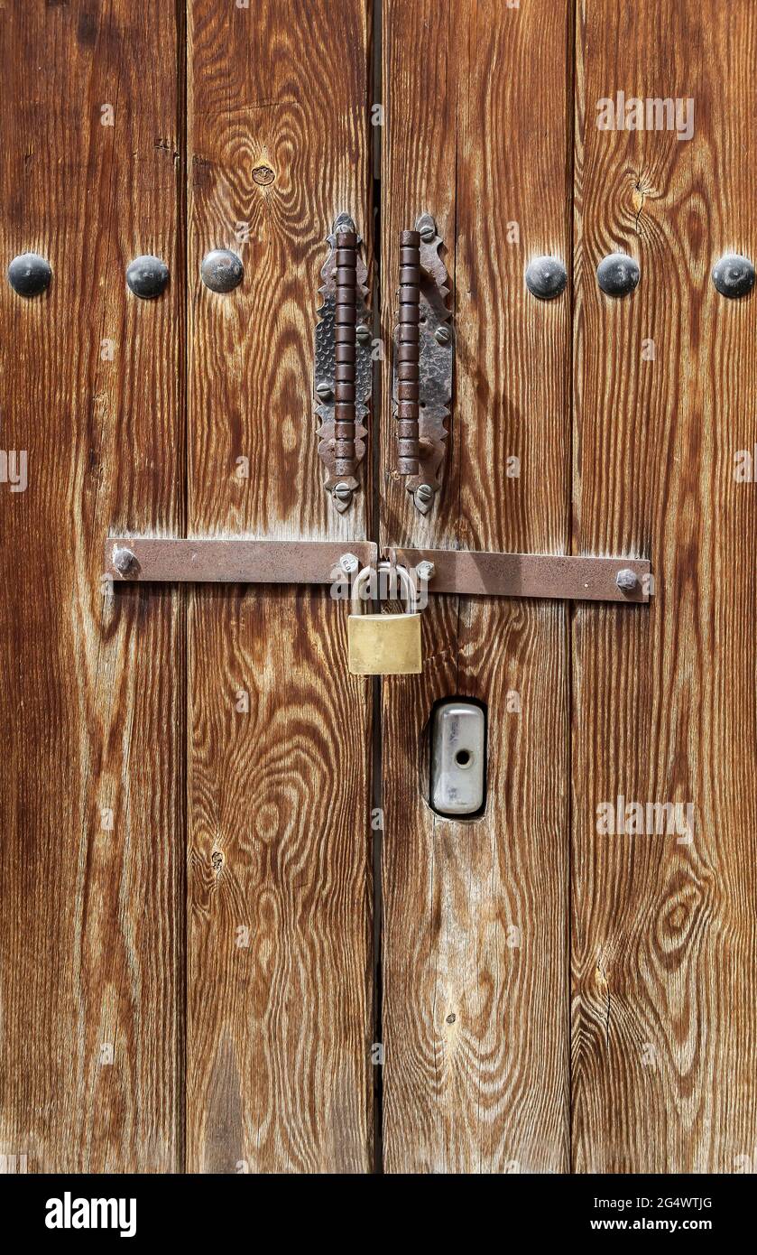 wooden door decorated with iron fittings closed with a padlock and a steel bar, forged handles, vertical Stock Photo