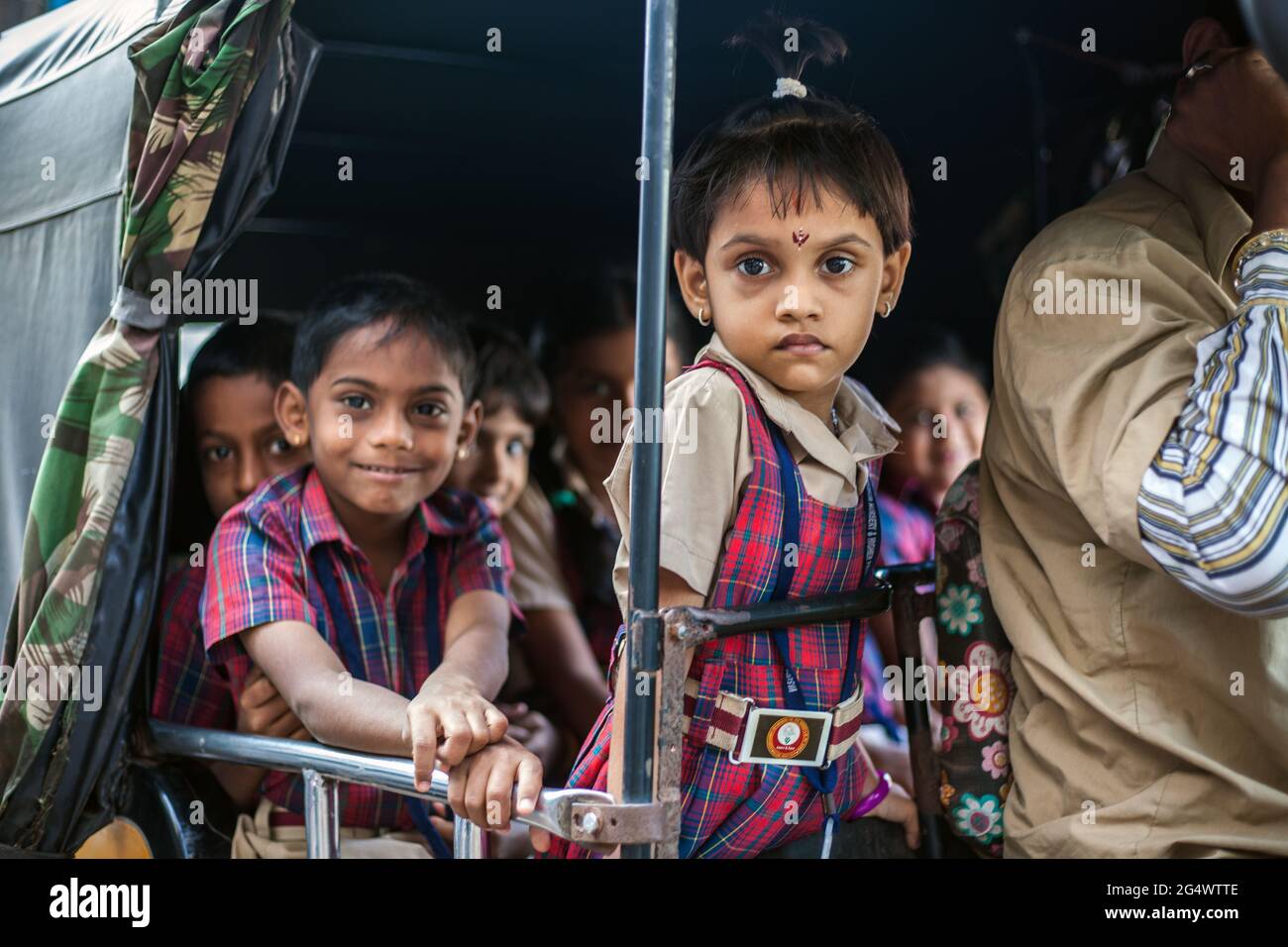 Cute young Indian schoolkids wearing check uniforms on school run in rear of auto rickshaw, Udupi, Karnataka, India Stock Photo