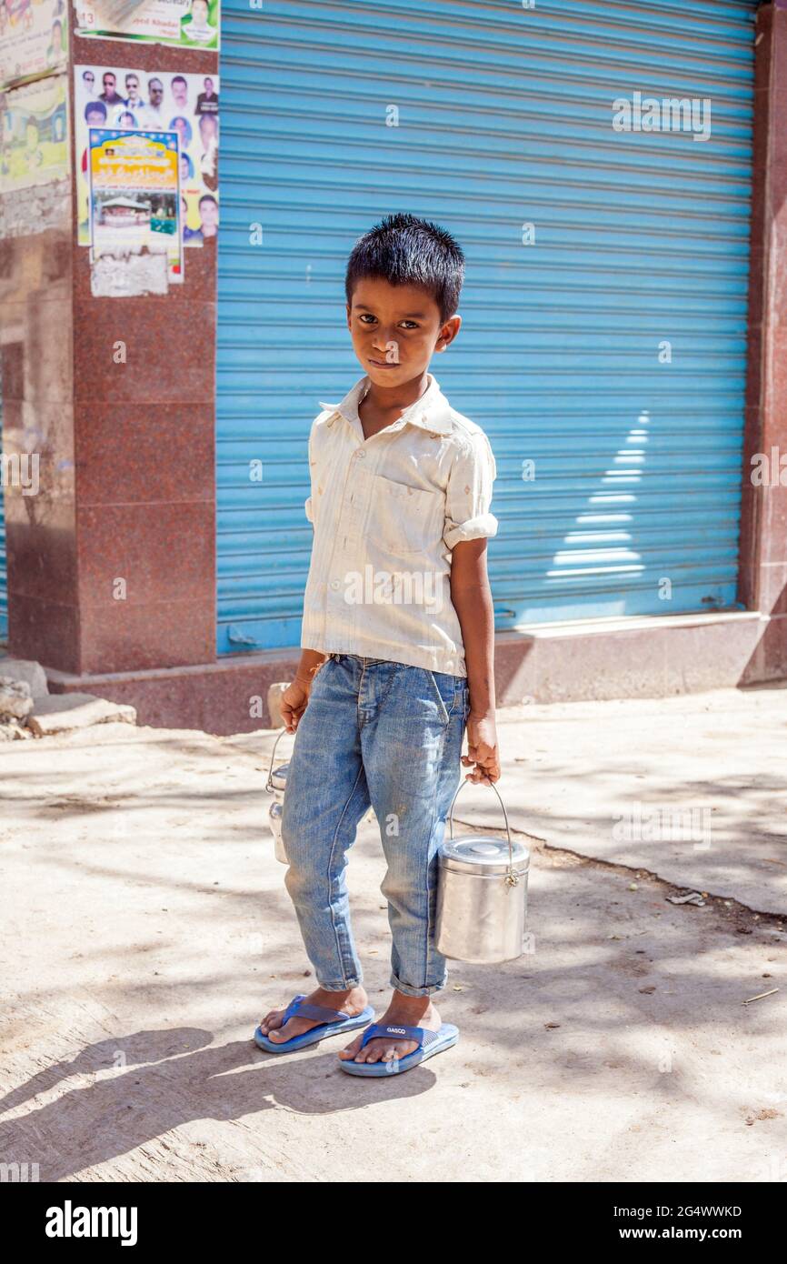 Cute young Indian lad wearing blue denim jeans with flip flops carries tiffin box in each hand, Mysore, Karnataka, India Stock Photo