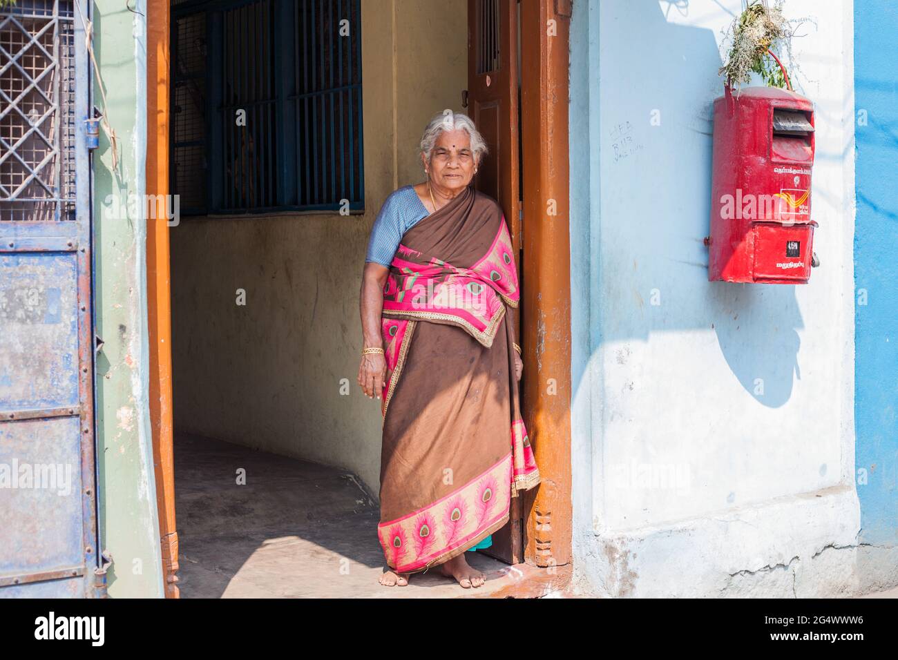 Indian lady poses in doorway beside red India Post letter box, Trichy, Tamil Nadu, India Stock Photo