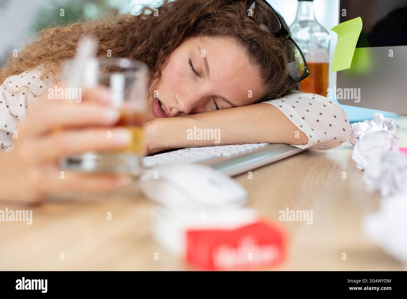 inebriated woman slumped across computer desk Stock Photo