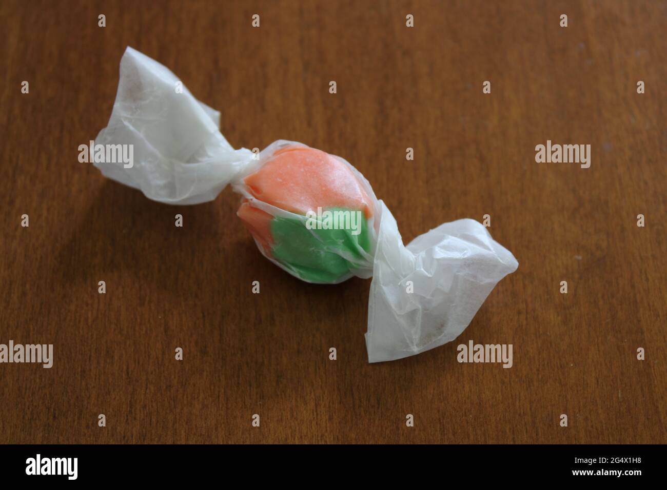 A Single Piece of Orange Flavor Old-Fashioned Saltwater Taffy Wrapped in Wax Paper Stock Photo