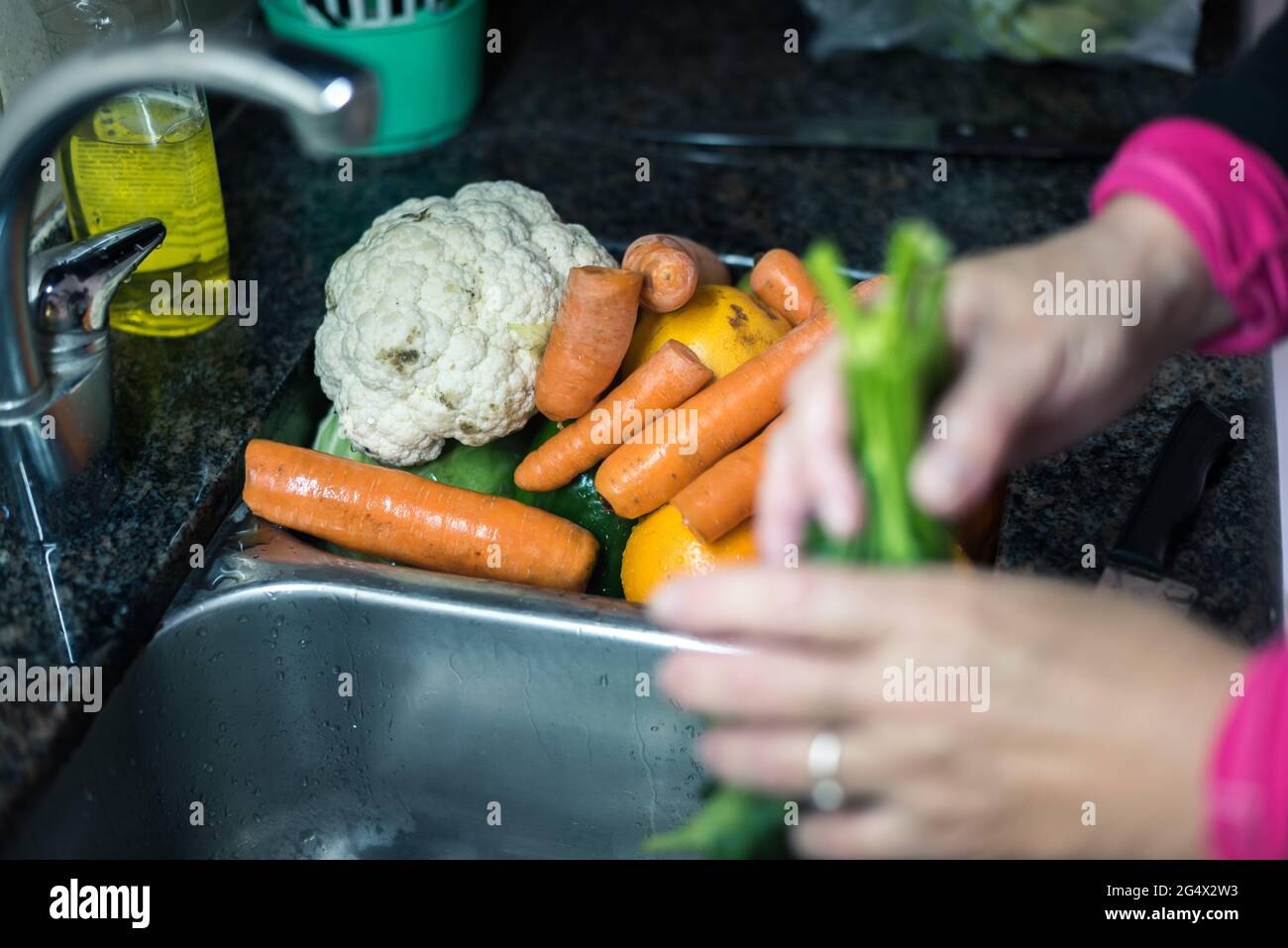 Mujer blanca lavando hojas y otros vegetales desde casa por la cuarentena, con agua en el fregadero de la cocina ,limpiando algunas fruta y verdura pa Stock Photo