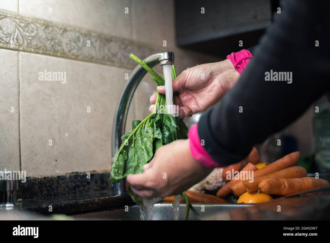 Mujer blanca lavando hojas y otros vegetales desde casa por la cuarentena, con agua en el fregadero de la cocina ,limpiando algunas fruta y verdura pa Stock Photo