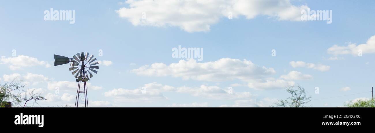 Fotografia del cielo tormentoso y tranquilo con nubes cumulus estractus azules, blancas, naranjas y negra , con un molino de agua de fondo, horizontal Stock Photo