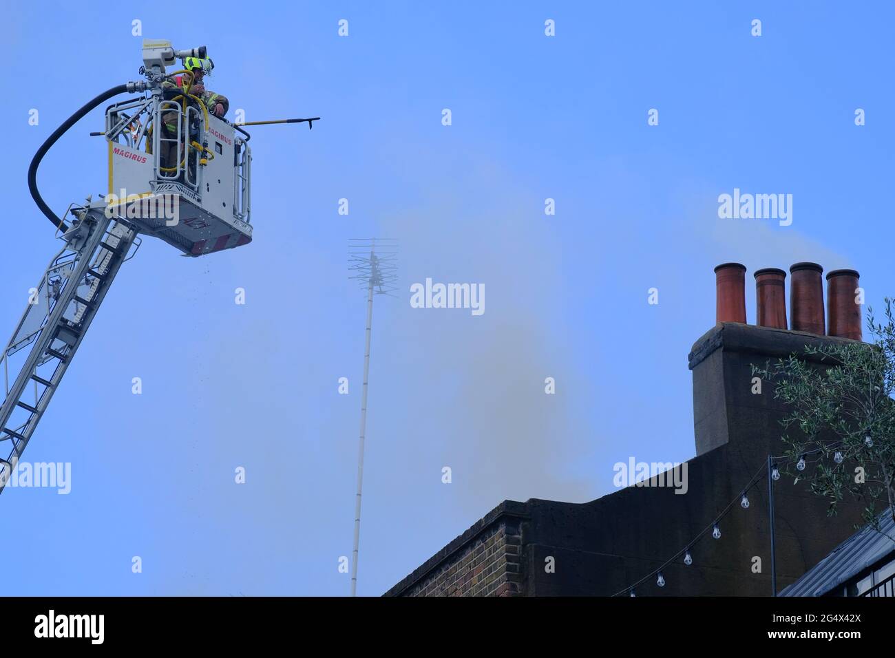 Firefighters on a hydraulic platform tackle a fire at a pub owned by Guy Ritchie, by piercing holes in the roof and directing water at the chimney Stock Photo