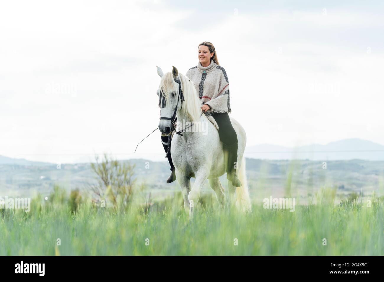 Smiling young woman riding horse at countryside Stock Photo