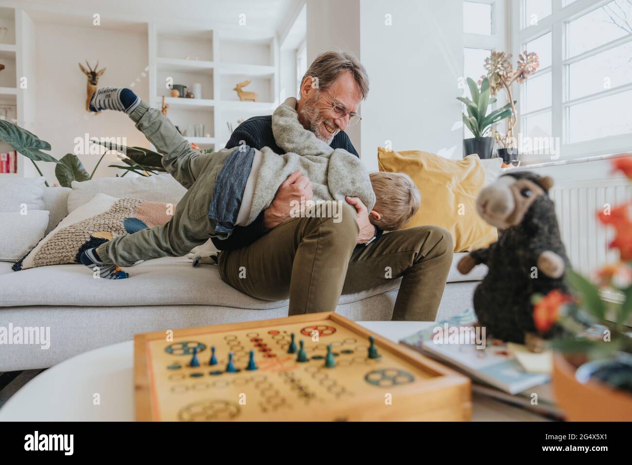 Son playing with father sitting on sofa at home Stock Photo