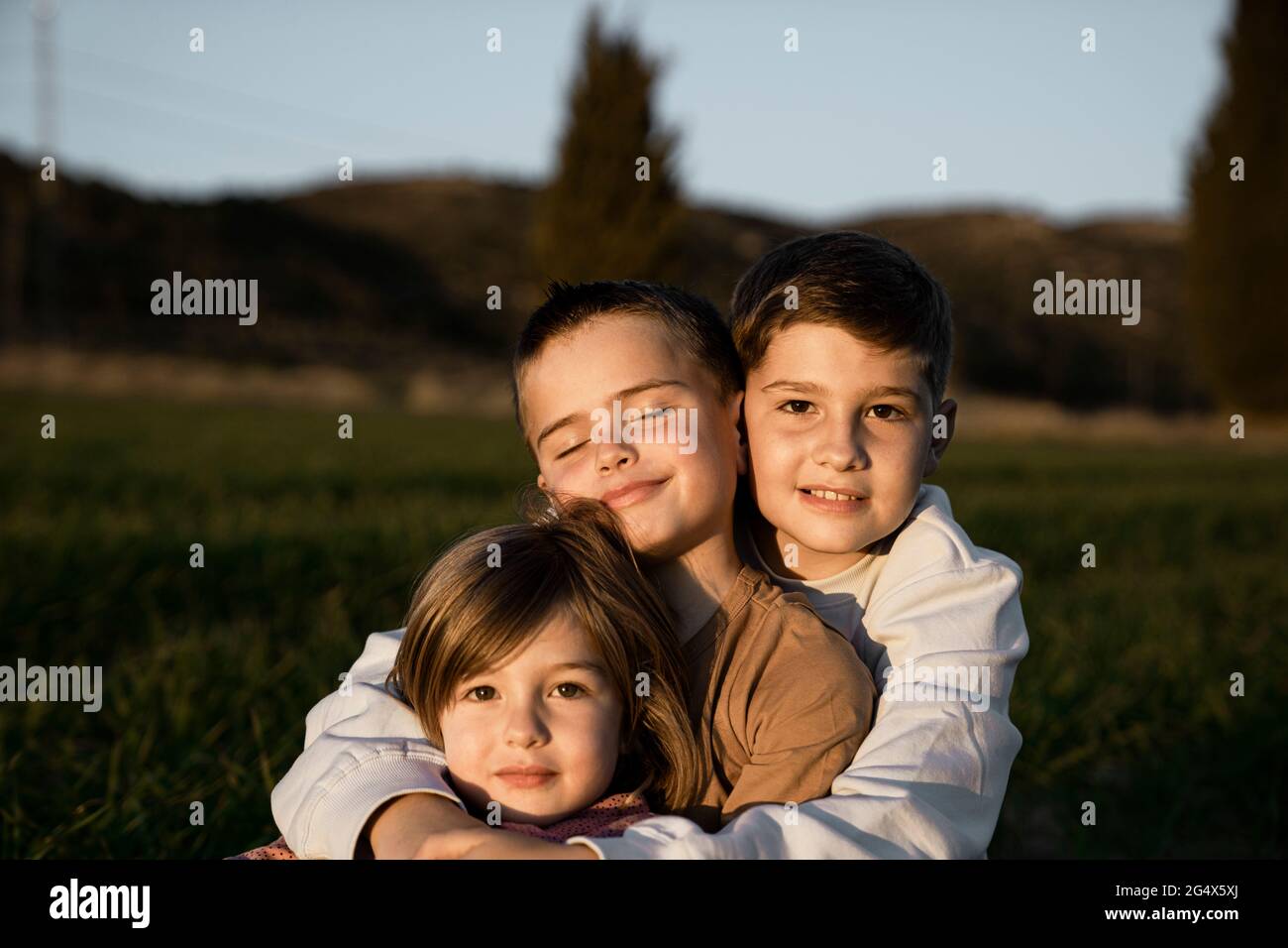 Brother and sister sitting with arms around at agricultural field Stock