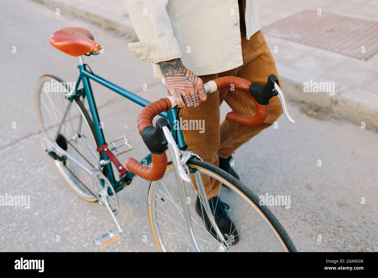 Tattooed man wheeling bicycle on road Stock Photo
