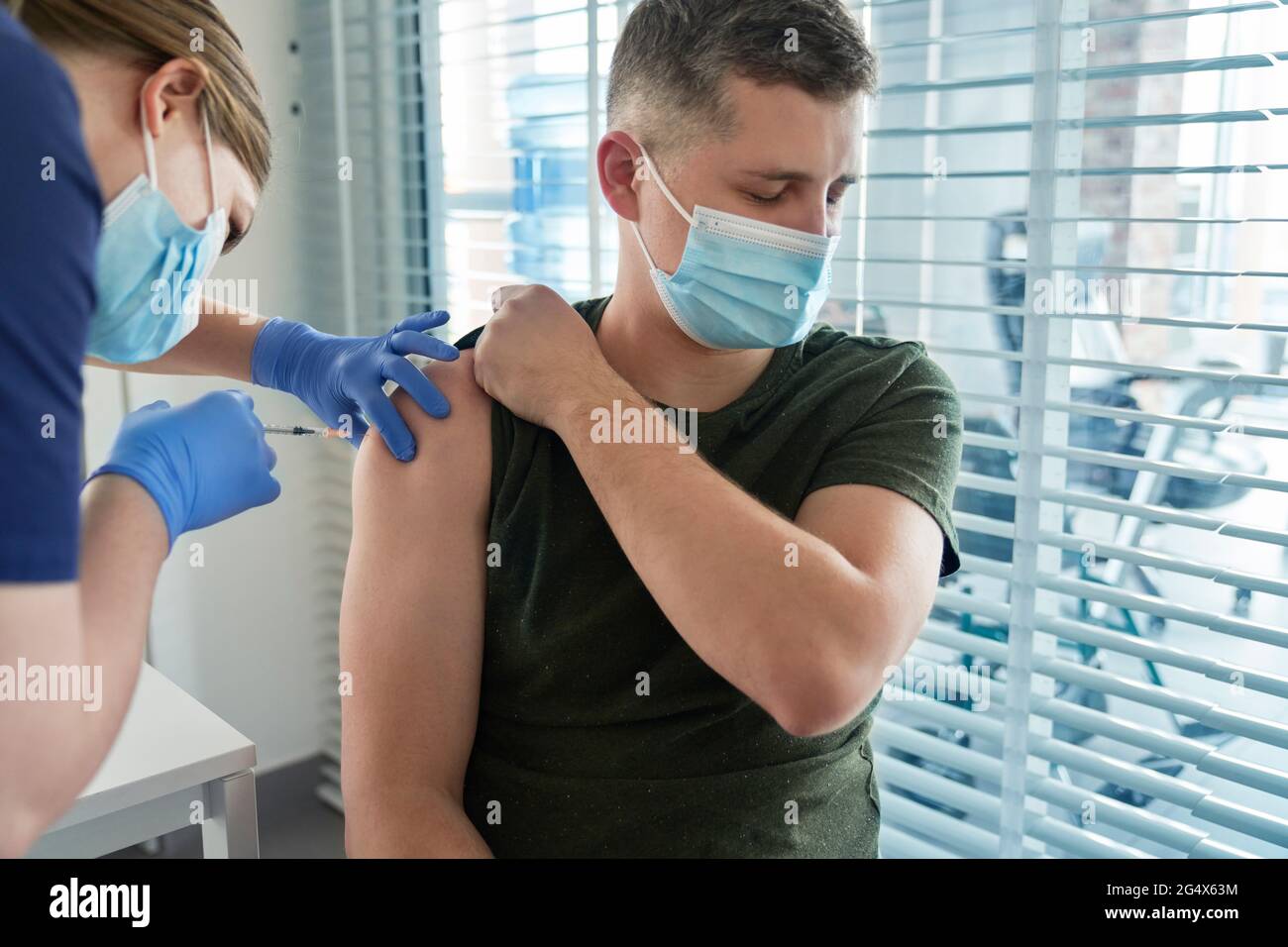 Female frontline worker injecting COVID-19 vaccine dose on arm of patient at center Stock Photo