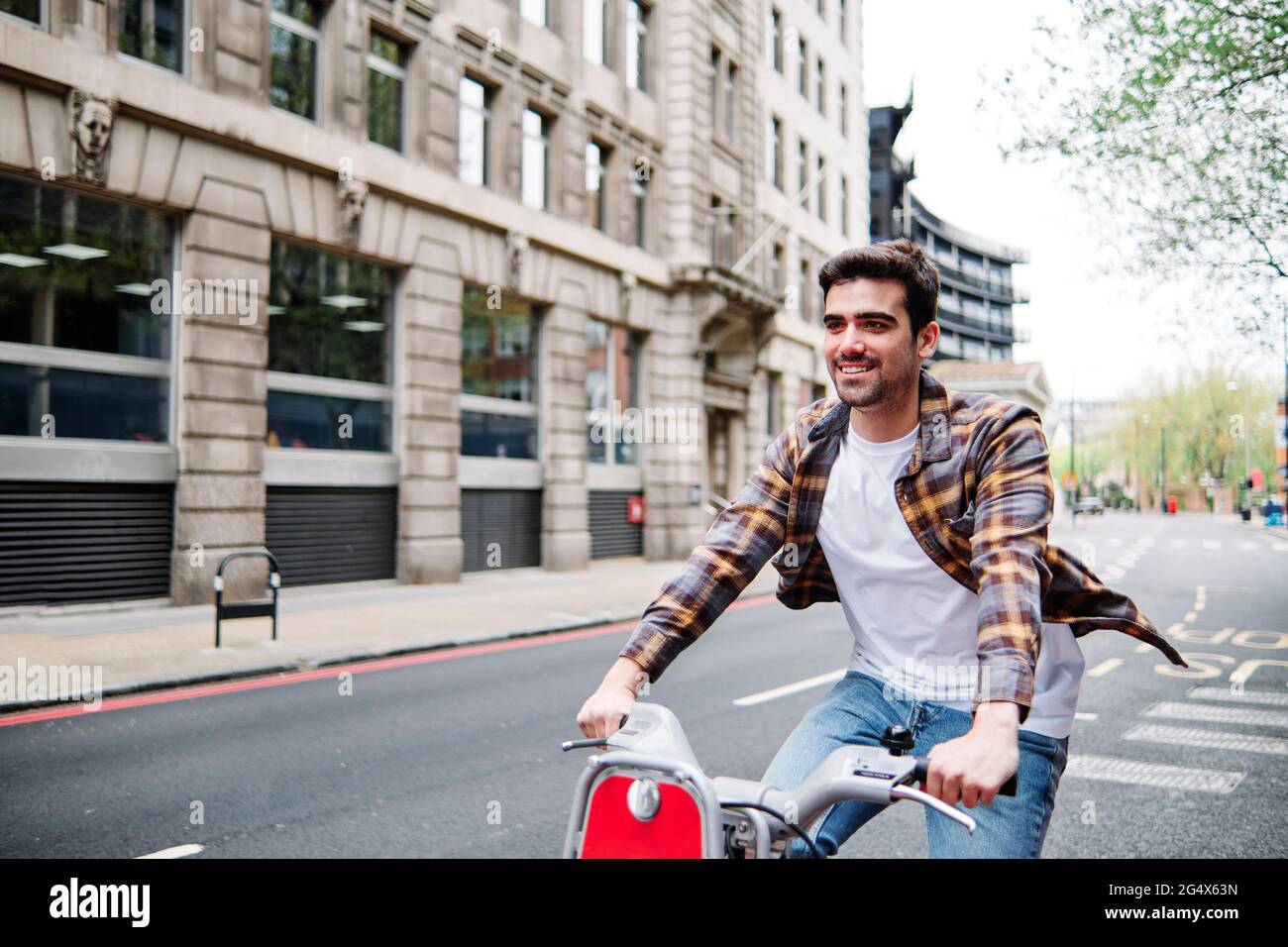 Smiling man wearing plaid shirt cycling on road in city Stock Photo