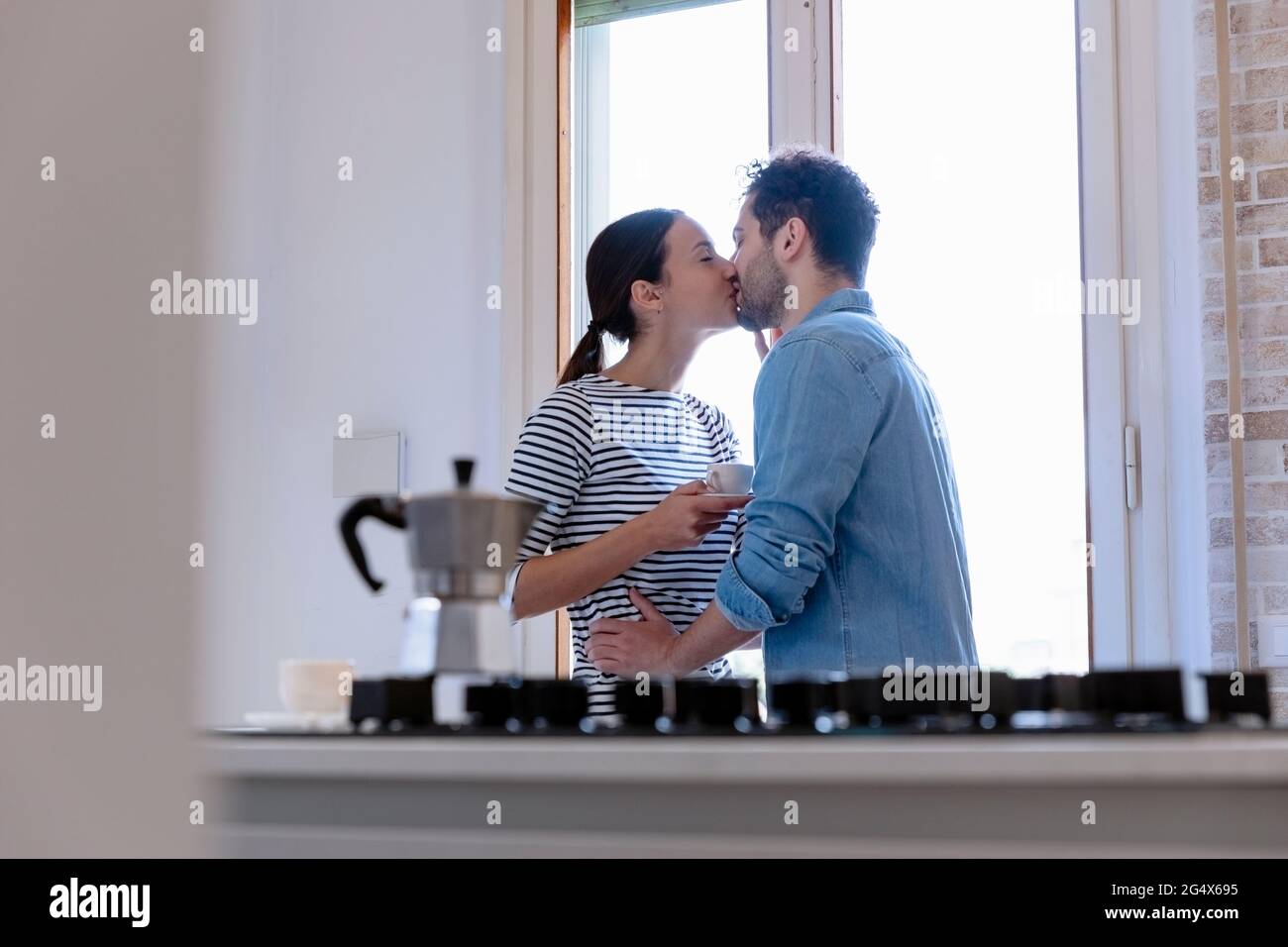 Couple kissing by window in kitchen at home Stock Photo