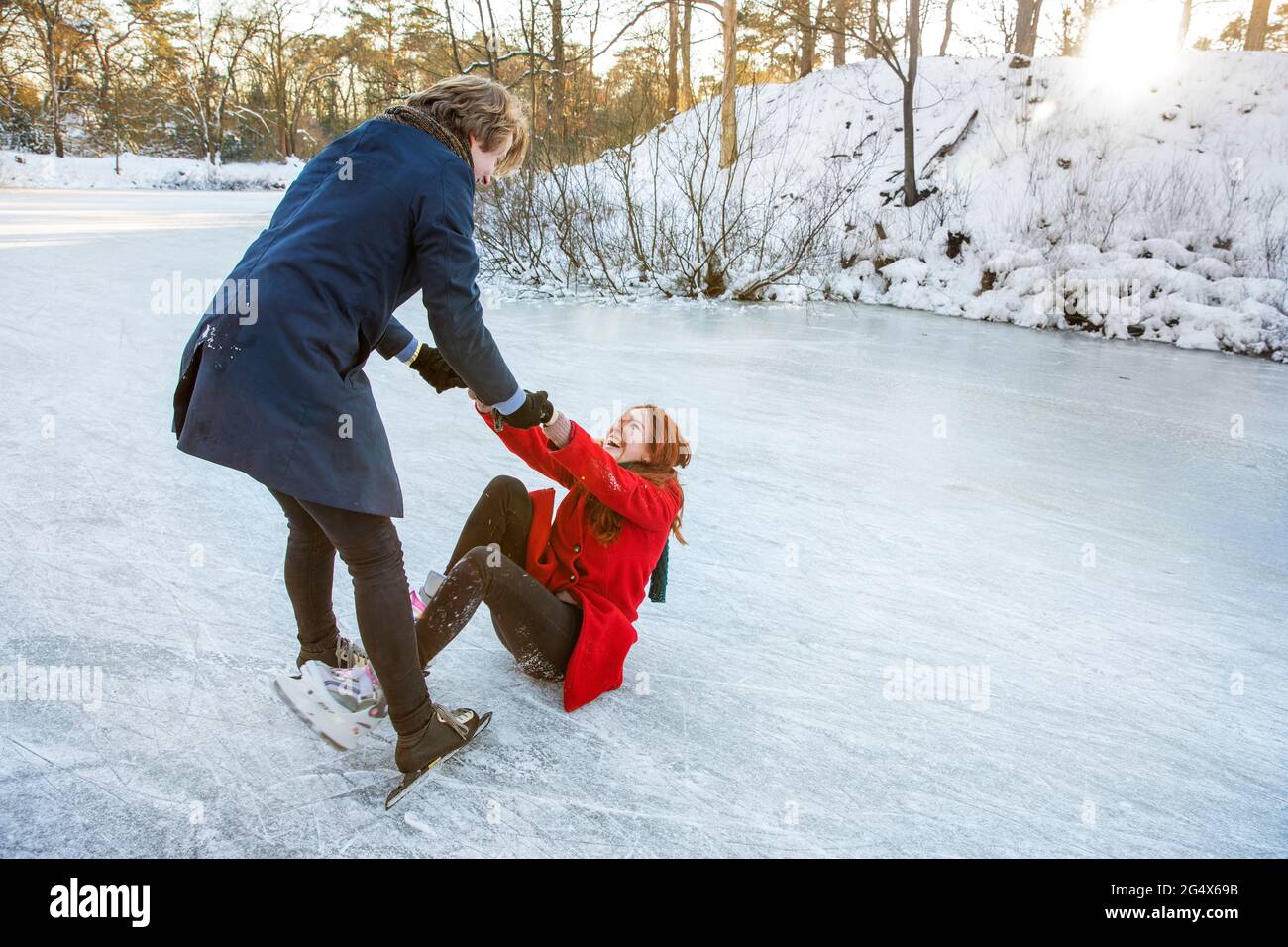 Boyfriend holding hands of girlfriend while getting up on frozen lake Stock Photo