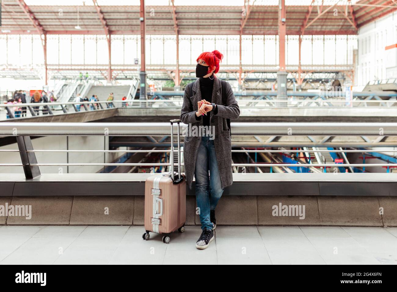 Redheaded woman with wheeled luggage waiting at railroad station Stock Photo
