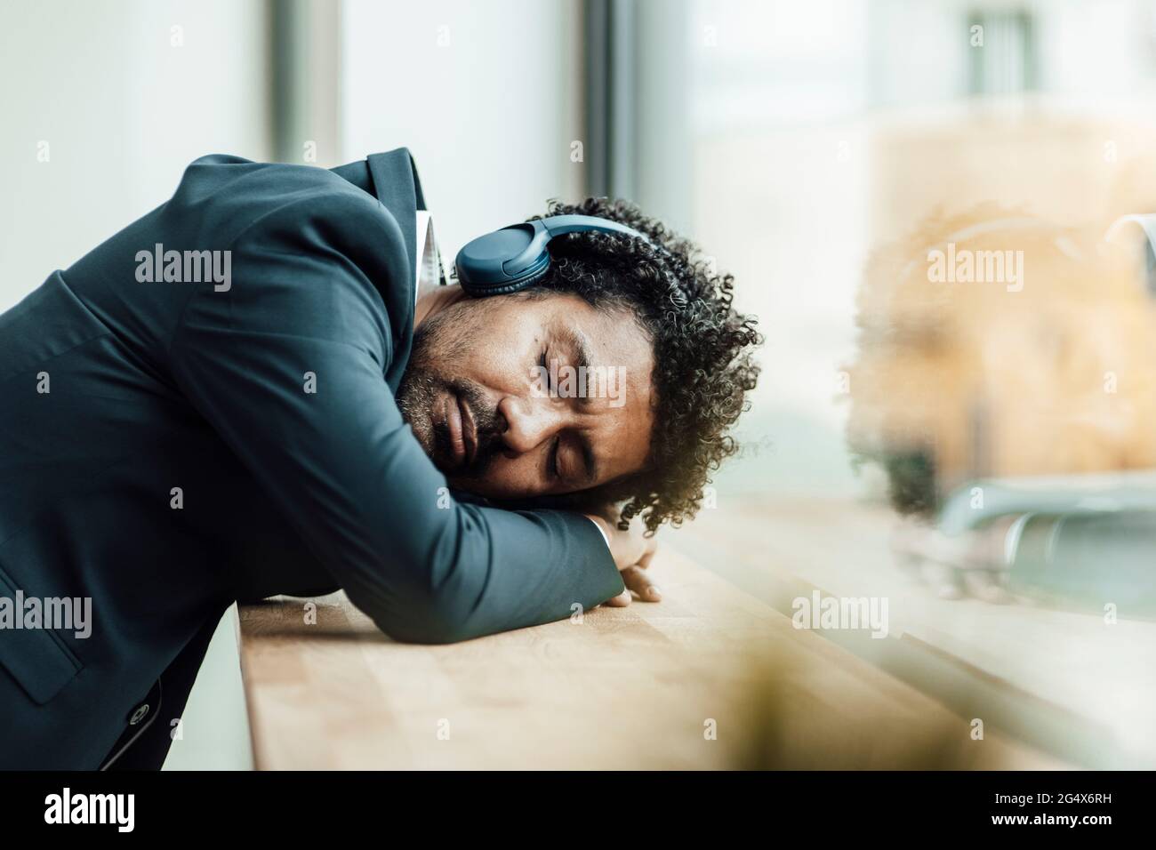 Mature businessman with eyes closed listening through headphones while resting head on desk in office Stock Photo