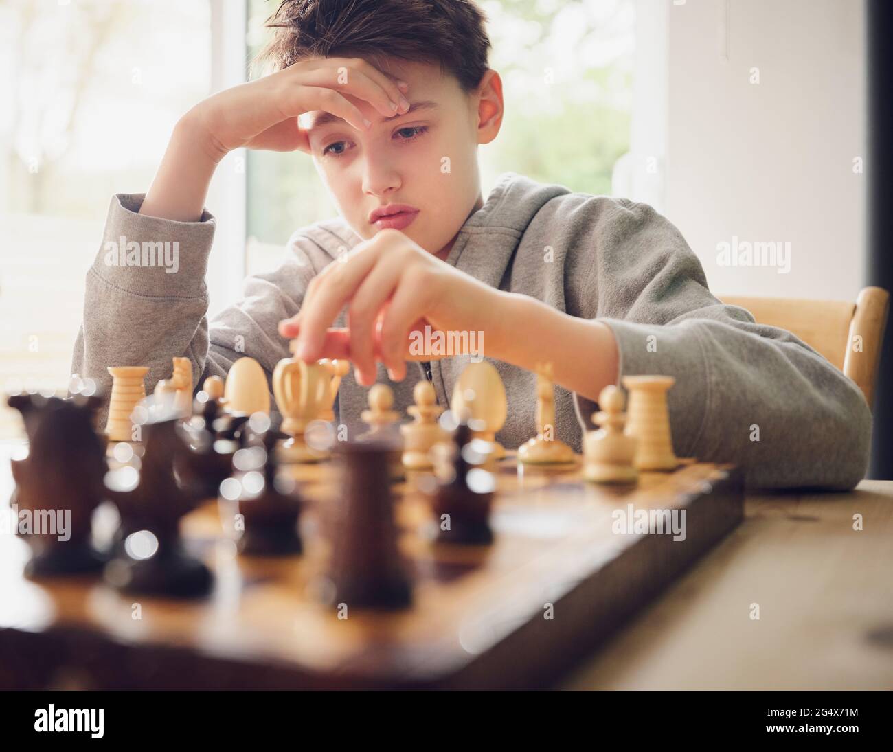 Boy with head in hand playing chess at home Stock Photo
