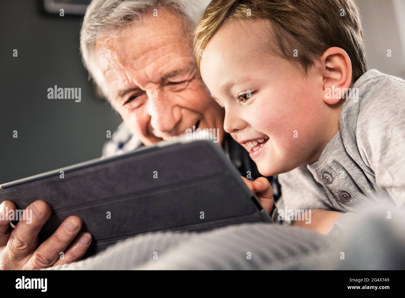 Smiling boy using digital tablet with senior man at home Stock Photo